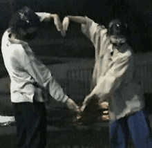 two people are making a heart shape with their hands while holding hands .