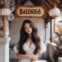 a woman in a white dress is standing under a sign that says balon168