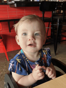 a baby girl wearing a blue shirt with palm trees on it sits at a table