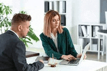 a man and a woman are sitting at a table in front of a laptop computer .