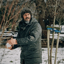 a man with a beard is standing in the snow near a tree with a sign that says ' etkinlik ' on it