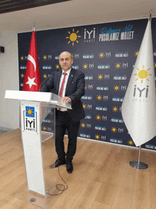 a man stands at a podium in front of a wall that has iyi parti written on it