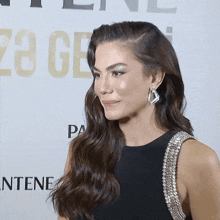 a woman wearing earrings and a black dress stands in front of a pantene sign