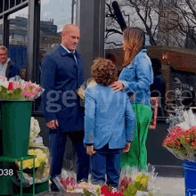 a man in a suit and tie stands next to a woman and a child in front of a flower shop