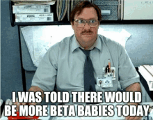 a man wearing glasses and a tie says i was told there would be more beta babies today in front of his desk