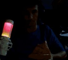 a man holding a slice of pizza in front of a microphone with a red light on it