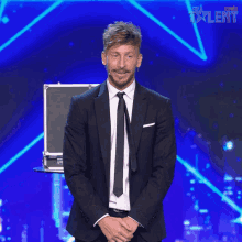 a man in a suit and tie stands on a stage in front of a sign that says " world talent "