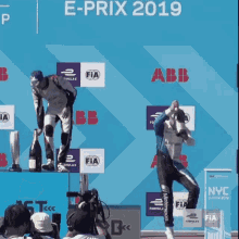 a man is standing on a podium with a bottle of champagne in front of a sign that says e-prix 2019