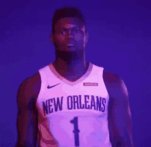 a basketball player wearing a new orleans jersey is standing in front of a purple background .