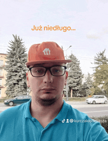 a man wearing glasses and an orange hat with the word już niedlugo on it