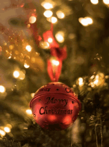 a red merry christmas bell is hanging from a christmas tree