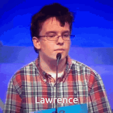 a young man in a plaid shirt stands in front of a microphone with the name lawrence written on the front of his shirt