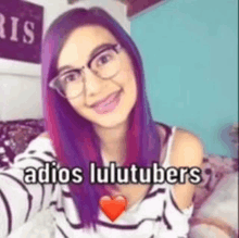 a woman with purple hair and glasses is taking a selfie with the words `` adios lulutubers '' .