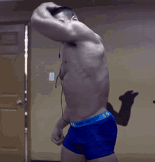 a shirtless man wearing blue under armour underwear flexes his muscles