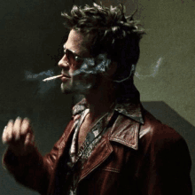 a man wearing sunglasses and a leather jacket is smoking a cigarette .