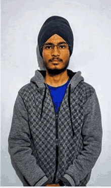 a man wearing a turban and a hoodie is standing in front of a white wall .