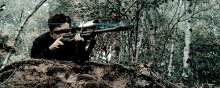 a man is aiming a rifle in the woods with trees in the background