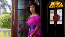 a woman in a purple dress is standing in front of a stained glass door .