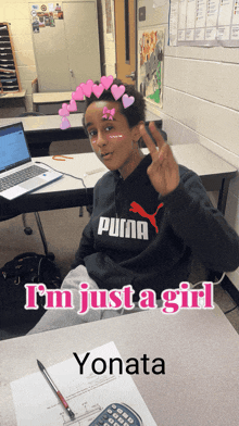 a boy wearing a puma sweatshirt sits at a desk in front of a laptop