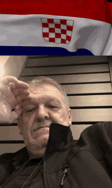 a man in a black jacket is sitting in front of a flag of croatia