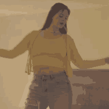 a woman wearing a yellow crop top and ripped jeans is dancing