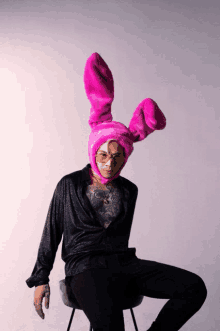 a man wearing a pink bunny hat and glasses sits on a chair