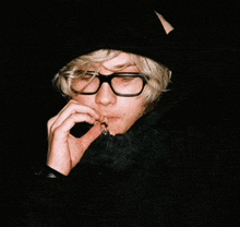 a man wearing glasses is smoking a cigarette in the dark