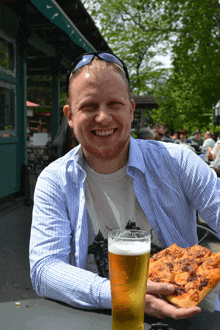 a man holds a slice of pizza and a glass of beer