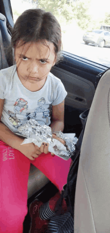 a little girl sitting in the back seat of a car holding a piece of tin foil