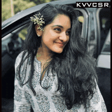 a woman with a flower in her hair is smiling in front of a black car with the letters kvvcsr above her