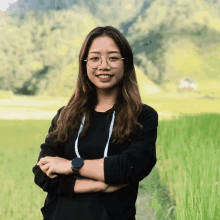 a woman wearing glasses and a watch stands in front of a grassy field