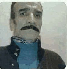 a man with a mustache is wearing a black jacket and a blue shirt .