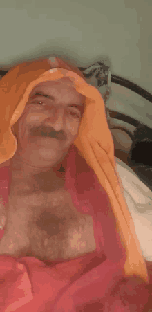 a man with a mustache is laying on a bed with an orange blanket covering his head