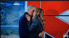 a man and a woman are kissing in front of a red abc sign