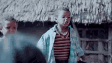 a group of children are standing in front of a thatched roof . one of the children is smoking a cigarette .