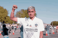 a man in a herbalife nutrition shirt holds his fist up in the air