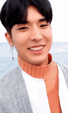 a young man wearing a sweater and earrings is smiling for the camera