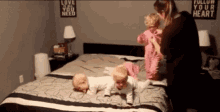 a woman is playing with three babies on a bed with a sign that says love is all you need on the wall behind them .