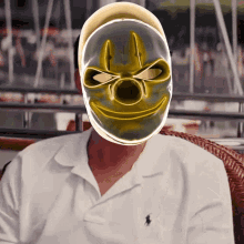 a man wearing a white polo shirt has a yellow clown mask on his face