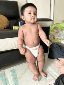 a baby in a diaper is standing on a mat and looking at the camera