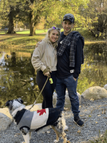 a man and woman standing next to a dog wearing a sweater with a maple leaf