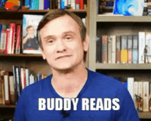 a man in a blue shirt says buddy reads in front of a bookshelf filled with books