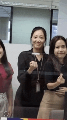 a group of women are standing next to each other in an office and making a heart shape with their hands .