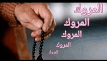 a person is holding a rosary in their hands with arabic writing on it .