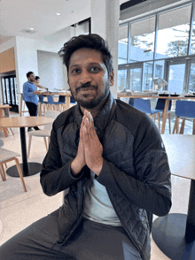 a man with his hands folded in prayer looks at the camera