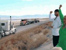 a man and a woman are standing in front of a semi truck on the side of a road .