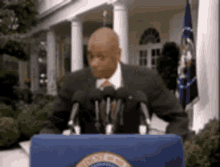 a man in a suit and tie is standing at a podium with microphones in front of a white house .