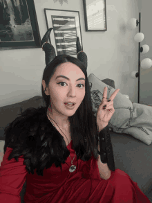 a woman in a red dress and black horns is sitting on a couch giving a peace sign