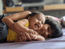 a baby in a yellow tank top is laying on a person 's lap and smiling