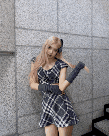 a woman wearing a plaid dress and gloves is standing in front of a brick wall